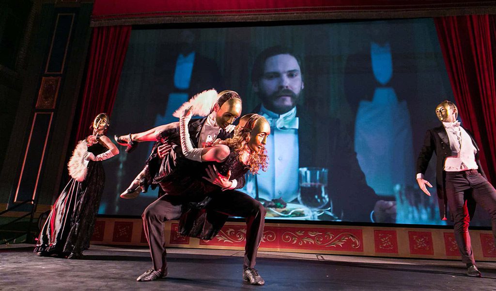 Dancers on Stage with Masks while clips from the show air on a big screen in the background.